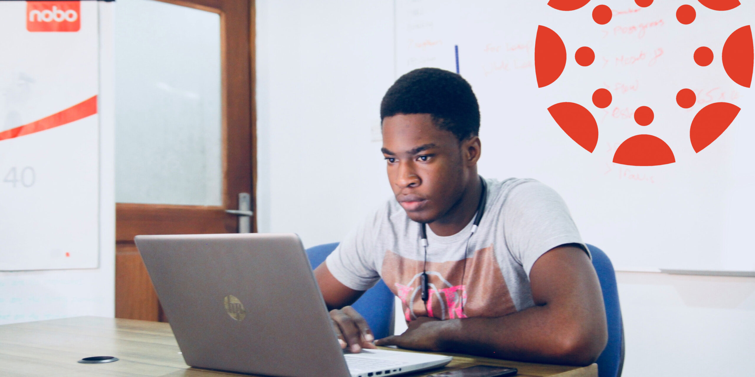 Student sitting behind a laptop computer with the Canvas logo over his shoulder.